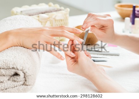 Closeup shot of a woman in a nail salon receiving a manicure by a beautician with nail file. Woman getting nail manicure. Beautician file nails to a customer. Royalty-Free Stock Photo #298128602