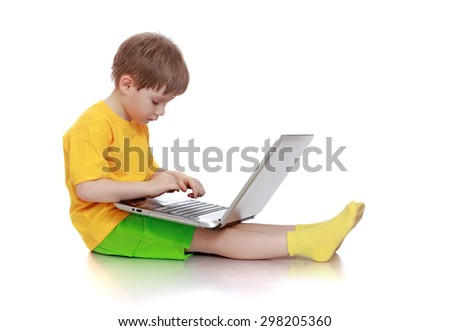  little boy in a yellow shirt and green shorts sitting on the floor and presses the button of the laptop-isolated on white background