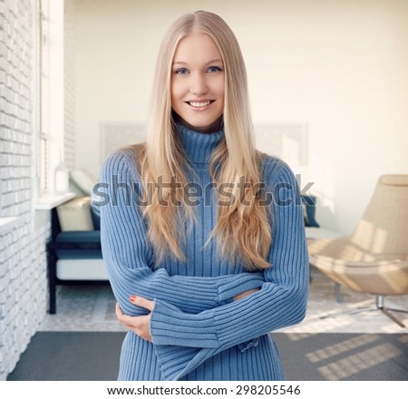 Happy blonde woman smiling arms crossed at stylish home.