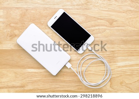Smartphone charging with power bank on wood board Royalty-Free Stock Photo #298218896