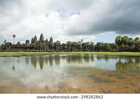 Ancient temple complex of Angkor Wat reflecting in still water under dramatic sky