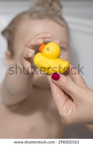 Little child sitting in bathroom with wet hair taking yellow duckling toy from hand of mother, vertical picture