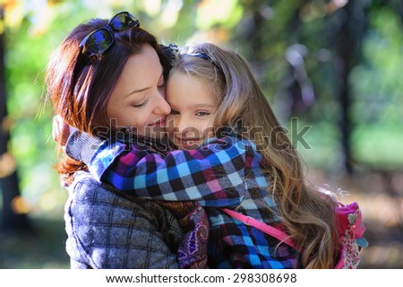 Young happy mother and little daughter hugging at autumn park background 