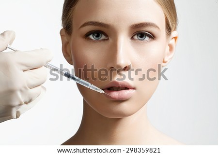 Beautiful girl doing an injection to increase the lips on a white background Royalty-Free Stock Photo #298359821