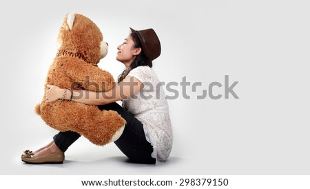 Sweet Asian girl looking each other to a teddy bear doll on her lap, over white background for copy space