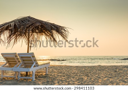 empty chairs under thatched umbrellas on a sandy beach Royalty-Free Stock Photo #298411103