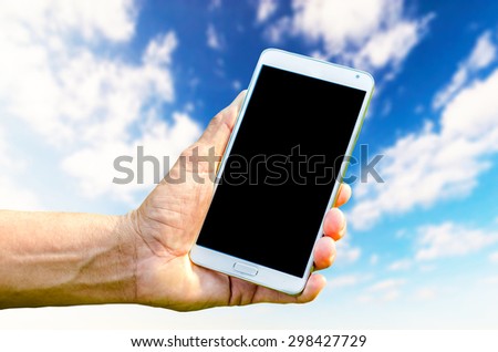 Man hand holding smartphone against on blue sky background soft focus.