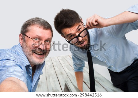 Two smiling colleagues taking the picture to them self sitting in the office, happy friends with glasses taking selfie with telephone camera  on white background