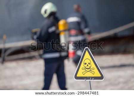 danger sign with skull and crossbones, firefighters on background