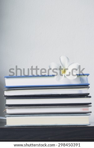 Stack of books and frangipani flower  on wooden table.