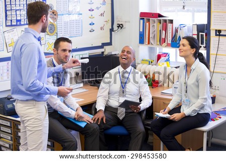 School teachers gather in a small school office for a chat. They look happy. A woman and three men group together. Royalty-Free Stock Photo #298453580