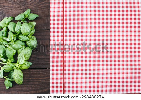 Green basil located on the right near a red and white cloth on a dark wooden background, close up
