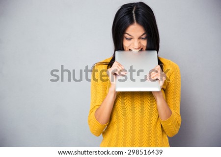 Angry woman biting tablet computer over gray background