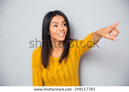 Cheerful young woman showing finger away over gray background
