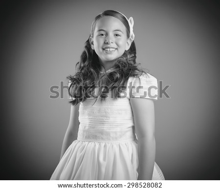 Beautiful young girl dressed in white. First Communion. Perfect teeth and smile, long curly hair. Dark background, studio shoot. Black & white picture.