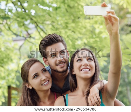 Cheerful smiling teens at the park sitting on a bench and taking selfies using a smart phone