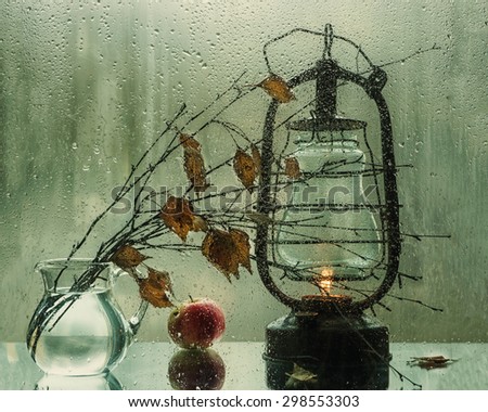 Still life with lantern behind the wet glass