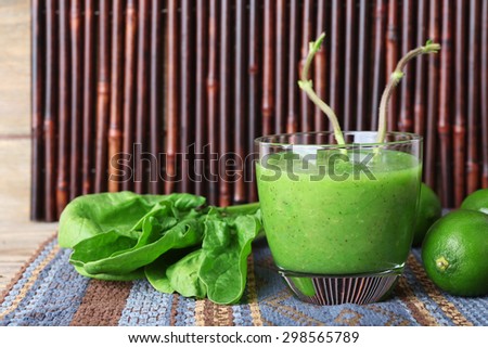 Glass of green healthy juice with spinach and limes on wooden background