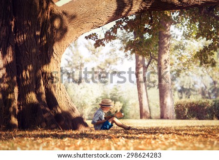 Golden afternoon dream. Boy reading book under big tree
