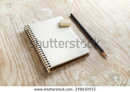 Sketchbook with a pencil and eraser on light wooden background with soft shadows. Template for graphic designers portfolios. Top view.