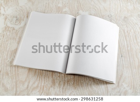Blank opened book on light wooden background with soft shadows. Template for graphic designers portfolios. Top view.