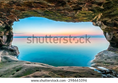 A sunset sky, reflected upon a calm Lake Superior, is framed by a sea cave along the Upper Peninsula coastline of Michigan.