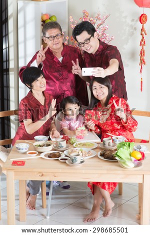Celebrating Chinese New Year, taking selfie at reunion dinner. Happy Asian Chinese multi generation family with red cheongsam dining at home.