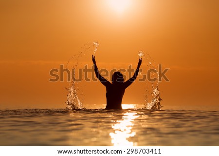 Beauty Model Girl Splashing Water with her hands. Teen girl Swimming and splashing on summer beach over sunset. Beautiful Woman in Water
