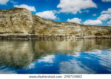 seascape, rocks against a blue sky with clouds reflected in the water