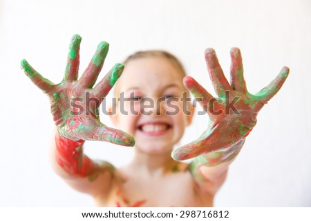 Little girl showing her hands, covered in finger paint after painting a picture and her body with it. Playfulness, creativity, permissive parenting, fun childhood concept, selective sharpness. 