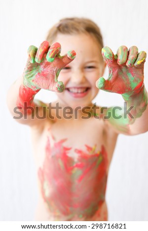Little girl showing her hands, covered in finger paint after painting a picture and her body with it. Tactile play, innovative learning, permissive upbringing, fun childhood concept, blur.