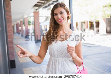 Portrait of smiling woman pointing the window and looking at camera at the shopping mall