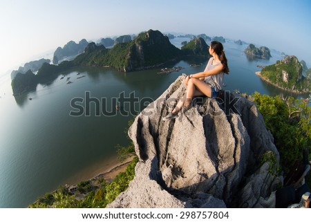 A young traveler girl sit on the top of mountain in Halong bay and enjoy the beauty of seascape. Young girl love wild life, travel, freedom. Royalty-Free Stock Photo #298757804