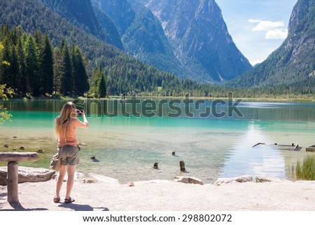 Nice girl taking photo with compact camera while on lake Toblach in south Tyrol, Italy