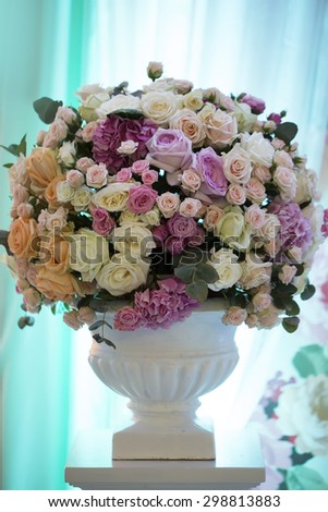 Decorative wedding bouquet of fresh beautiful flowers of roses and peony white pink violet purple yellow lilac and orange colours in big vase on blue curtain background, vertical picture