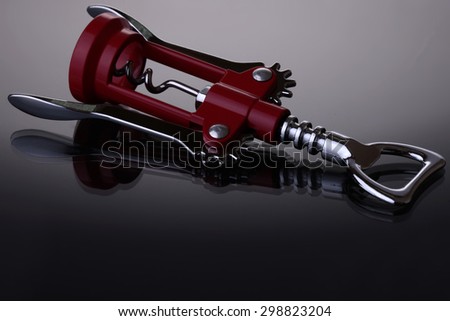 One elegant corkscrew made of red plastic and bright metallic base with spiral lying on reflecting surface in studio on black glossy background copyspace, horizontal picture
