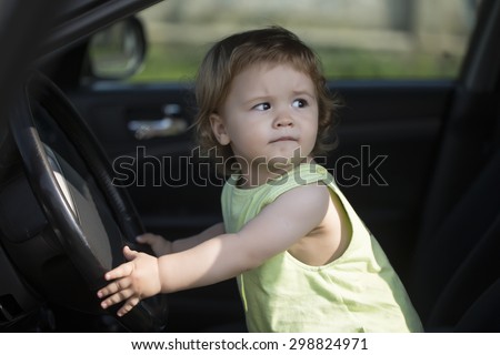 Beautiful little curious male kid driver sitting in big car with black salon holding wheel looking away through window in summer, horizontal picture