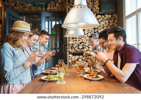 people, leisure, friendship, technology and internet addiction concept - group of happy smiling friends with smartphones taking picture of food at bar or pub