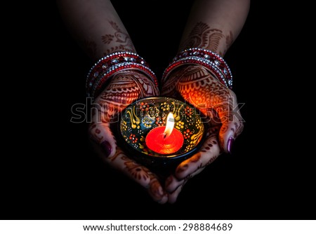 Woman hands with henna holding lit candle isolated on black background with clipping path 