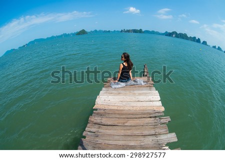 A young traveler girl sit on the wooden bridge in Halong bay and enjoy the beauty of seascape.