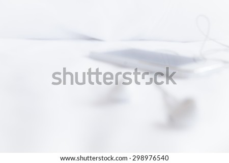 Blurred headphones and phone on white sheet, blurred texture background.