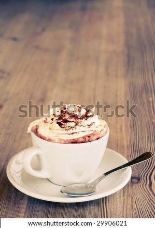 A cup of hot chocolate with cream on a wooden textured table