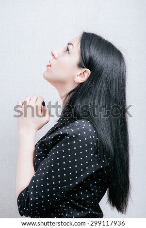 Beautiful woman praying to God. On a gray background.