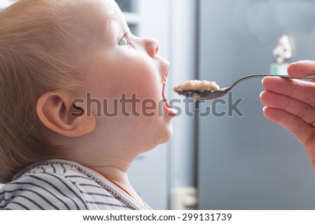 Mother feeds baby boy with a spoon porridge Royalty-Free Stock Photo #299131739