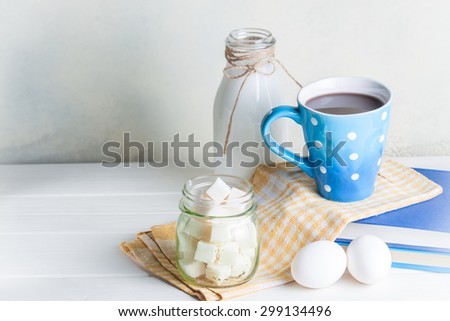 Blue cup of coffee with eggs and bottle of milk on white background