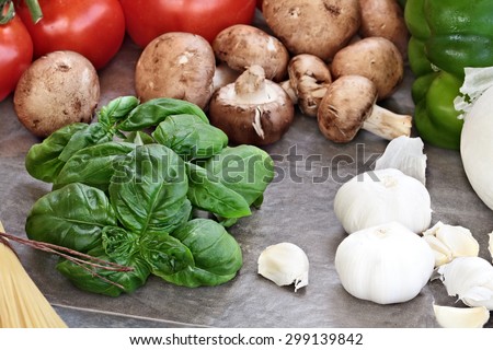 Italian cuisine ingredients of fresh basil leaves, garlic, mushrooms, onions, peppers and fresh tomatoes, Selective focus on basil with extreme shallow depth of field.