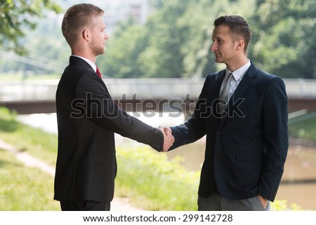 Happy Businessmen Shaking Hands While Standing Outdoors In Park