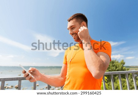 fitness, sport, people, technology and healthy lifestyle concept - smiling young man with smartphone and earphones listening to music at summer seaside