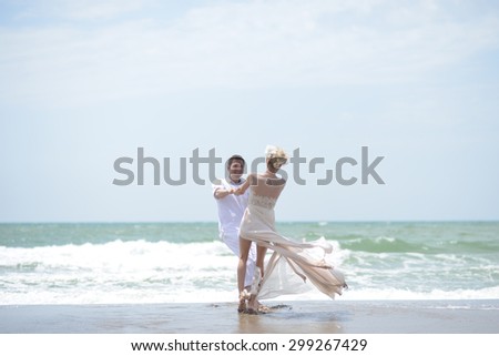 Pretty happy young wedding couple of boy and girl in white spinning on ocean beach coast on windy weather sunny day outdoor on blue sky background, horizontal picture