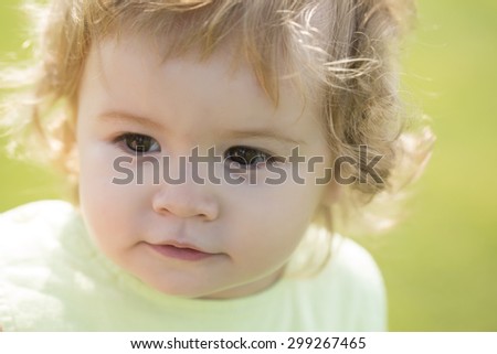 Portrait of small curious beautiful male child with blonde curly hair looking away outdoor sunny day on natural green background, horizontal picture